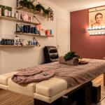 Cabine de soin d'un institut de beauté à Genève avec table de massage, étagères de produits et mur bordeaux