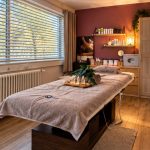 Salle de massage relaxant de Cledelweiss Institut à Genève : table drapée de serviettes, plateau de bougies et plante verte, murs bordeaux